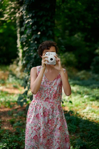 Sonriente chica tomando fotos en cámara instantánea en el bosque — Foto de Stock