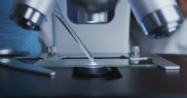 Teknisyen, mikroskop altında detaylı inceleme için cam kaydırağa pipetten bir çözelti damlatıyor..