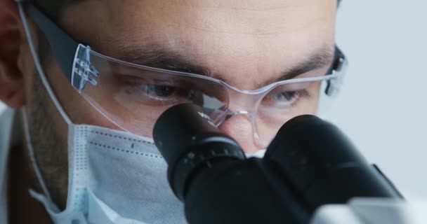 Científico joven mira bajo el microscopio . — Vídeos de Stock