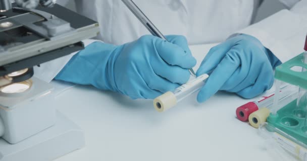 Asistente de laboratorio firma tubos de ensayo de pluma para recoger análisis e investigación adicional — Vídeo de stock