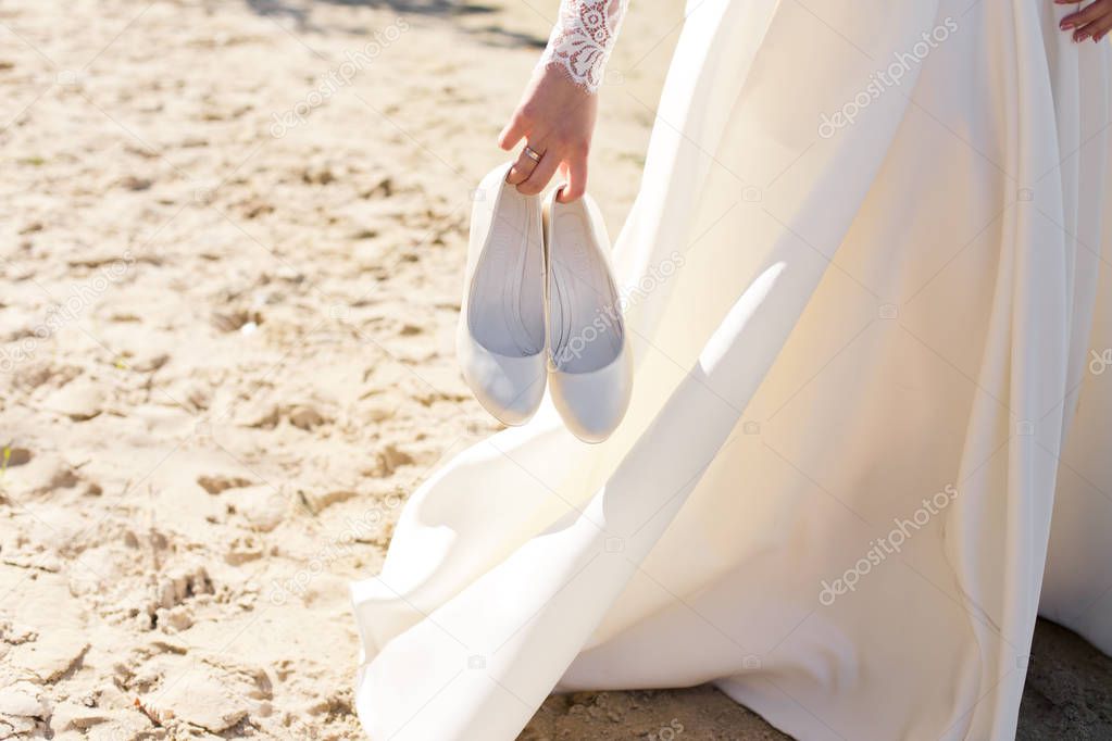 Wedding warm white shoes in brides hands on the beach.