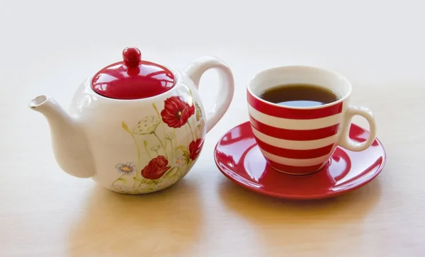 Striped cup with tea on a saucer and brewer with a poppy picture — Stock Photo, Image