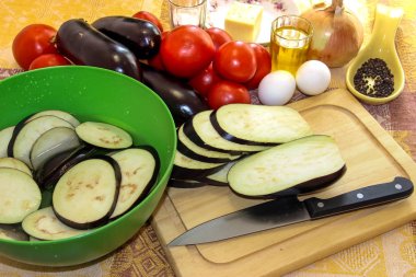 Bir kesme tahtası ve sırılsıklam içinde tuzlu suda dilimlenmiş patlıcan