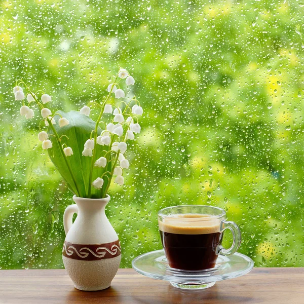 Uma chávena de café e lírios do vale na janela. Chuva cai na janela . — Fotografia de Stock