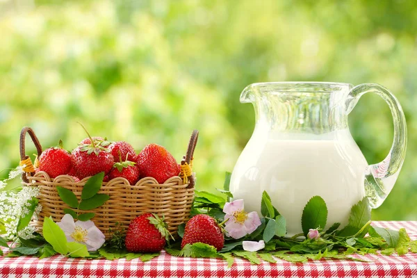 Клубника в плетеной корзине и кувшин молока. Натюрморт в летнем саду. Размытый фон . — стоковое фото