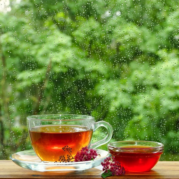 A cup of tea and flower honey by the window. It is raining outside the window. Glass in the drops of rain. — Stock Photo, Image