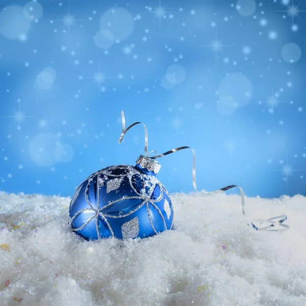 Blue New Year\'s ball in the snow. Christmas card with blue ball on a blue background.