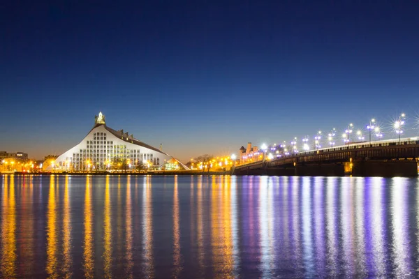 Prachtige nacht zicht op Letse nationale bibliotheek en stenen brug over de rivier Daugava in Letland Riga. Nacht, Xmas verlichte scène. — Stockfoto