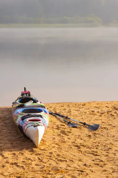 Kayak coloré avec pagaies et gilet de sauvetage sur une plage du nord avec forêt brumeuse en arrière-plan le jour d'été. Vue panoramique sur sable blanc, eau claire bleue. Leningrad région Saint-Pétersbourg Russie . — Photo