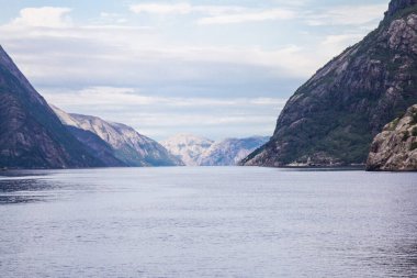 Güneşli bir günde, dağ zirvelerinin yeşil yamaçları, su yüzeyleri ve gökyüzünde tüy bulutları olan manzarası. Neroyfjord - Norveç 'in en dar fiyordu, Gudvangen Flam