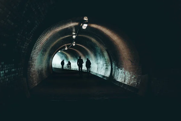 人们在黑暗的城市隧道的剪影去光 人们走在黑暗隧道的灯光下 — 图库照片
