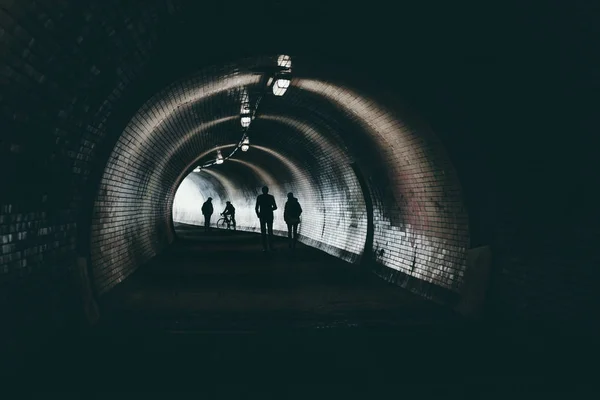 People silhouette in dark urban tunnel goes to the light . People walking to the light in dark tunnel .