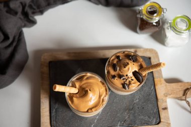 Dalgona kahvesi, modaya uygun bir içecek. Tahtada iki bardak Dalgona kahvesi