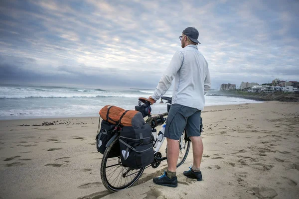 Junger Mann mit gepacktem Fahrrad am Strand — Stockfoto