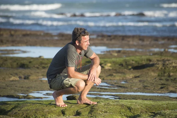 Homem senta-se em seus honches em rochas pelo oceano — Fotografia de Stock