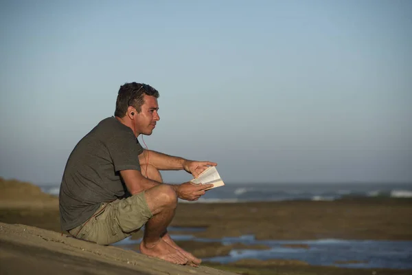 Man met oortelefoons en boek door Oceaan — Stockfoto