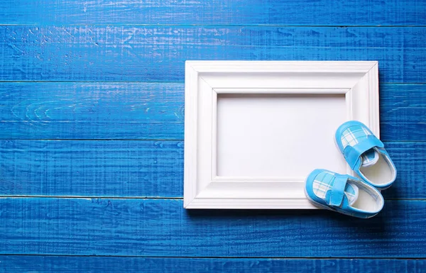 Bootees de bebé con un marco sobre un fondo azul — Foto de Stock