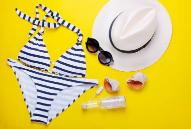 Şık mayo, şapka, güneş gözlüğü ve kabukları sarı bir arka plan üzerinde