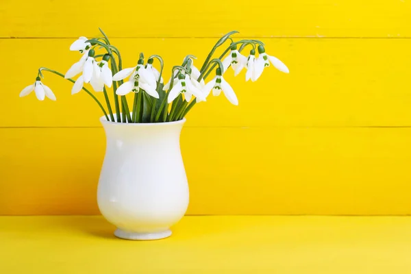 黄色の背景の上に白い花瓶の Snowdrops — ストック写真