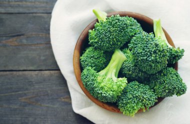 Ahşap bir masa üzerinde bir yuvarlak ahşap kase taze brokoli.