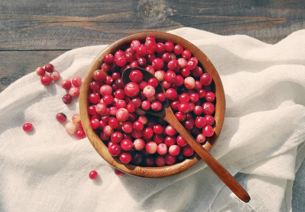 Canneberge rouge fraîche dans un bol rond avec une cuillère en bois sur un tissu de lin blanc sur une surface de table . — Photo