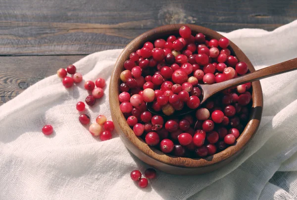 Canneberge rouge fraîche dans un bol rond avec une cuillère en bois sur un tissu de lin blanc sur une surface de table . — Photo