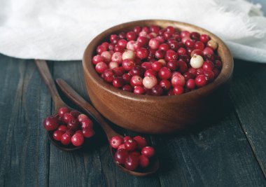 Taze kırmızı orman kızılcık masa yüzeyi beyaz keten kumaş üzerine bir tahta kaşıkla bir yuvarlak kase.