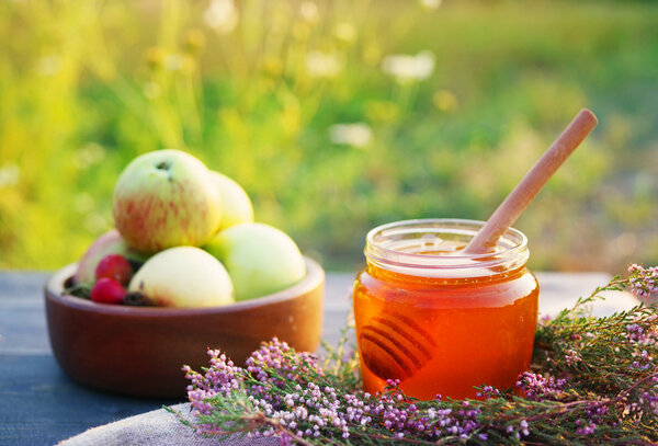 Honey in a glass jar with flowers melliferous herbs and autumn apples