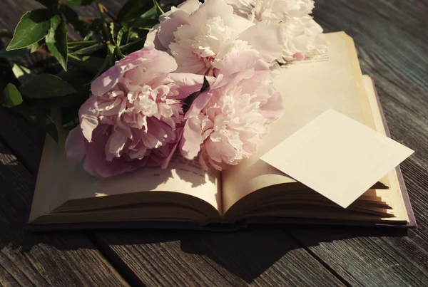 Ramo de peonías rosadas en un libro abierto una tarjeta blanca vacía para el texto — Foto de Stock