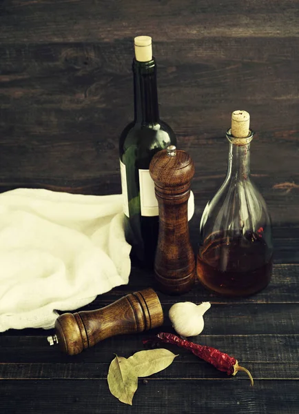 Wine in a bottle, balsamic vinegar, pepper mill of wood and garlic on a wooden surface — Stock Photo, Image