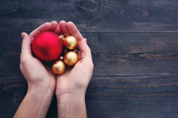 Vermelho e yelllow rodada bolas de Natal em mãos masculinas sobre fundo de madeira rústica . — Fotografia de Stock
