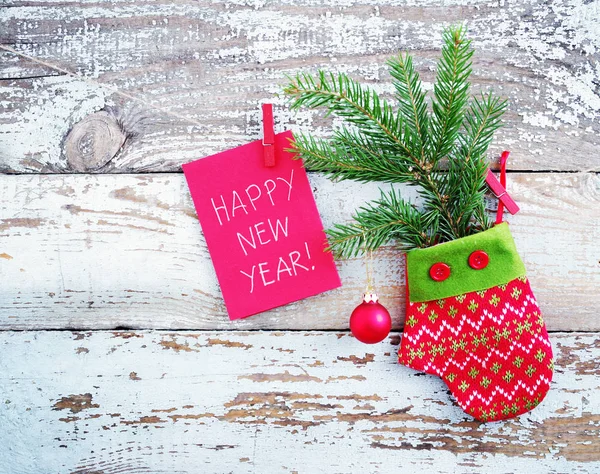 Manopla roja decorativa, rama de abeto con una bola y una tarjeta roja con la inscripción "Feliz Año Nuevo" en una cuerda contra el fondo de la vieja tabla eliminada — Foto de Stock