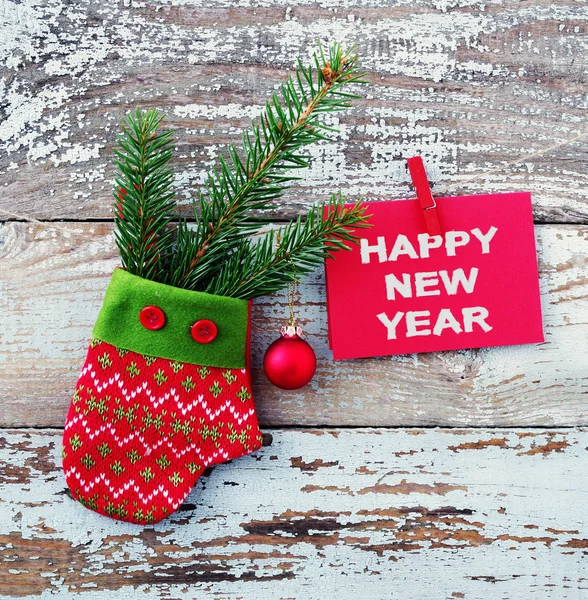 Manopla roja decorativa, rama de abeto con una bola y una tarjeta roja con la inscripción "Feliz Año Nuevo" en una cuerda contra el fondo de la vieja tabla eliminada —  Fotos de Stock