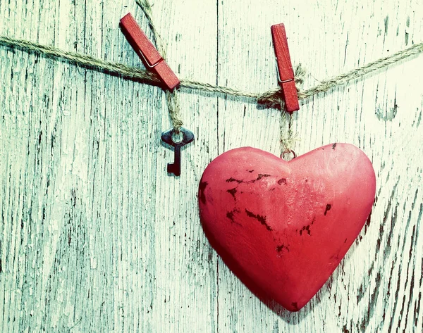 Coração vermelho decorativo e pequena chave de metal em uma corda contra o fundo de uma placa branca velha, close-up, tom vintage . — Fotografia de Stock