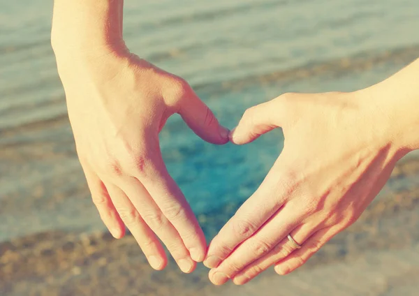 Mani femminili sotto forma di cuore contro il mare . — Foto Stock