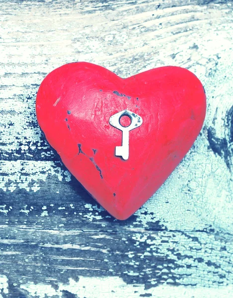 Coração vermelho e pequena chave de metal em um fundo velho de madeira . — Fotografia de Stock