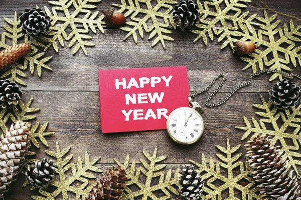 Noel ahşap arka plan dekoratif kar taneleri, çam kozalakları, eski saat ve yazıt "Happy New Year ile kırmızı kart ile". — Stok fotoğraf