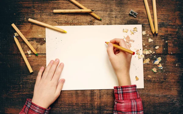 Çocuğun üzerinde boş beyaz bir kağıt yaprağına ve ahşap renkli kalemler yapılmış eski ahşap yüzeyde eller.. — Stok fotoğraf