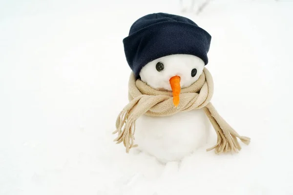 Bir kap ve bir eşarp kışın karda küçük kardan adam. — Stok fotoğraf