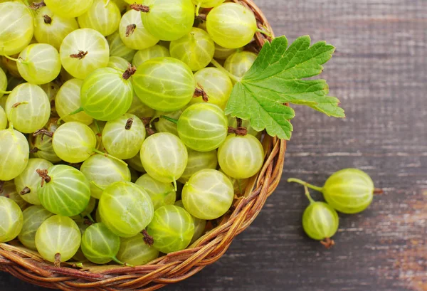 Juicy ripe berries of a gooseberry in a small basket on a wooden surface. — Stock Photo, Image