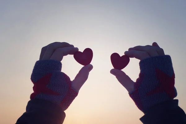 Twee decoratieve rode harten in vrouwelijke handen tegen de achtergrond van de hemel. Romantische achtergrond — Stockfoto