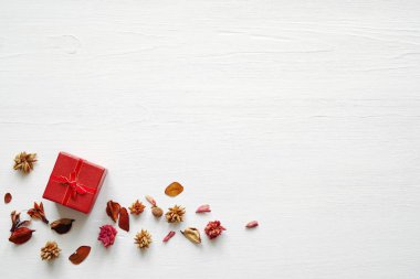 Beyaz ahşap zemin üzerinde kuru kokulu çiçeklerin bir ortamda bir yay ile kırmızı hediye kutusu. 