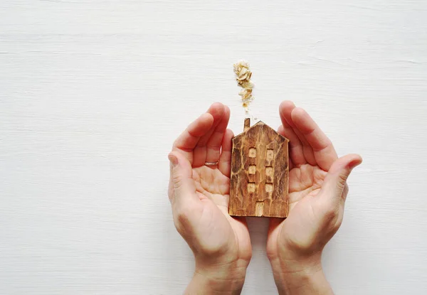 Wooden house in the woman's hands on a white wooden background. — Stock Photo, Image