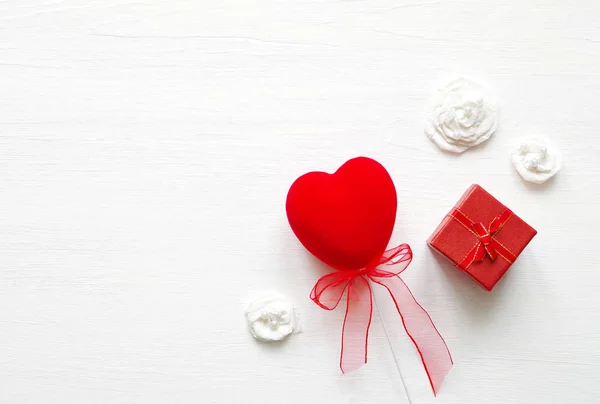 Piros szív és ajándék egy íj, egy fából készült fehér alapon piros négyzet. Romantikus kártya. — Stock Fotó