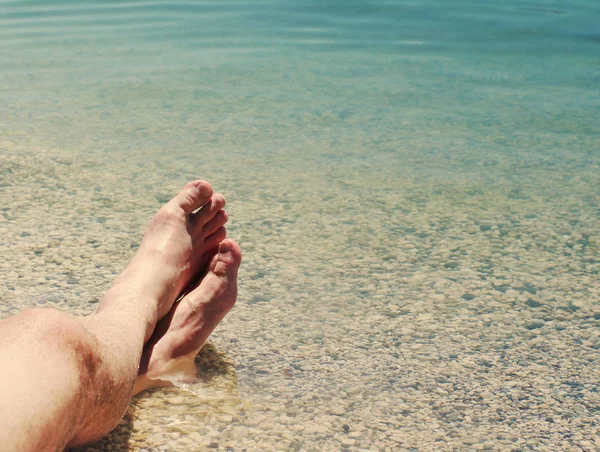 Mannelijke voeten op een strand tegen de zee in een zonnige zomerdag. — Stockfoto