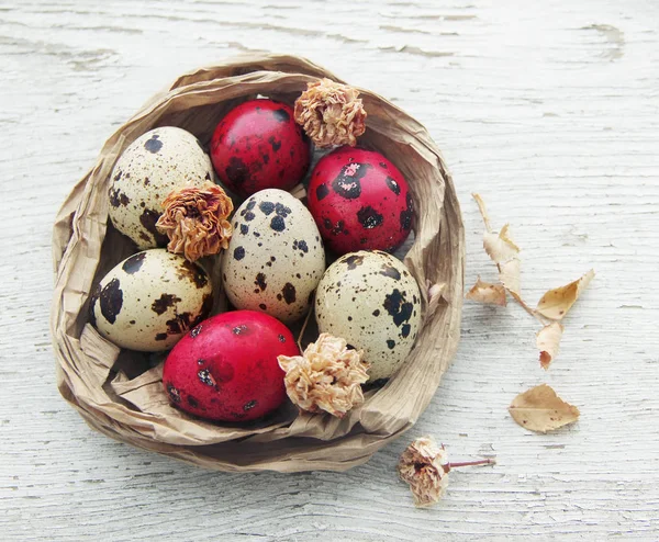 Uova di quaglia bianche e rosse pasquali in un nido decorativo sul vecchio tavolo dipinto in legno . — Foto Stock
