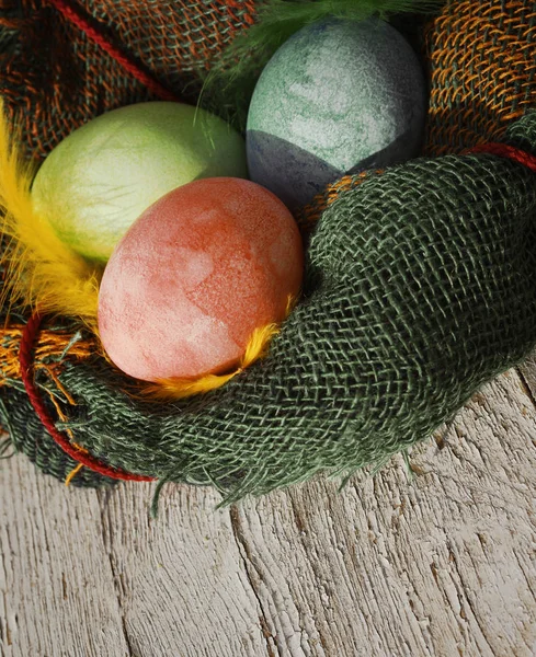 Easter eggs in a decorative nest with feathers on old wooden background — Stock Photo, Image