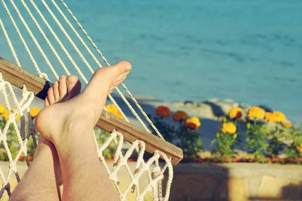 Manliga ben i en hängmatta på stranden mot havet i en solig sommardag. — Stockfoto