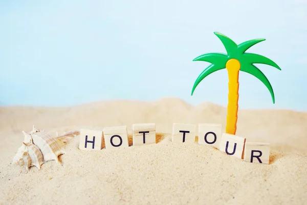 Text "HOT TOUR" from wooden letters and a toy palm tree in sand — Stock Photo, Image