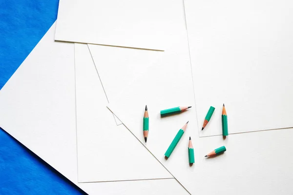 Ark av vitt papper och pennor på en blå bakgrund — Stockfoto